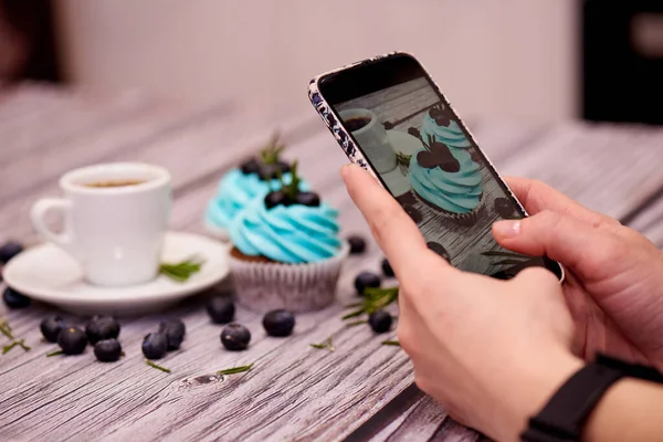 Food photography for the blog. Female hands shoots a photo of cupcakes on a smartphone.Food blogger shoots coffee and cupcakes. Food blog. Selective focus.