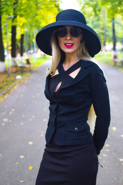 一位身穿黑色西装 头戴黑色帽子 头戴一瓶水的优雅的年轻女子漫步在阳光明媚的城市 — 图库照片