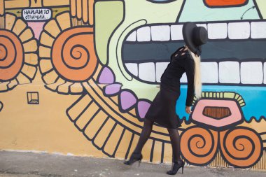 Siyah takım elbiseli ve siyah şapkalı zarif bir kadın. Yazın güneşli şehirde bir şişe su gezintisi yapıyor.