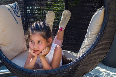 Küçük bir kız hasır bir sandalyede dinleniyor.