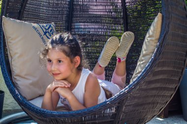 Küçük bir kız hasır bir sandalyede dinleniyor.