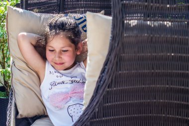 Küçük bir kız hasır bir sandalyede dinleniyor.