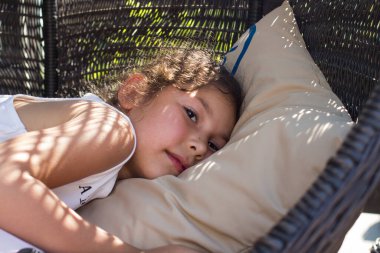 Küçük bir kız hasır bir sandalyede dinleniyor.