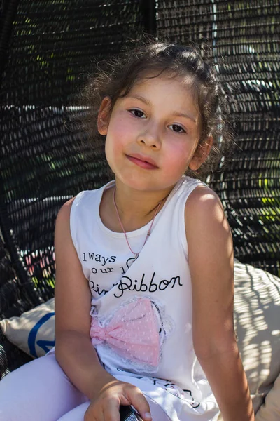 Küçük bir kız hasır bir sandalyede dinleniyor.