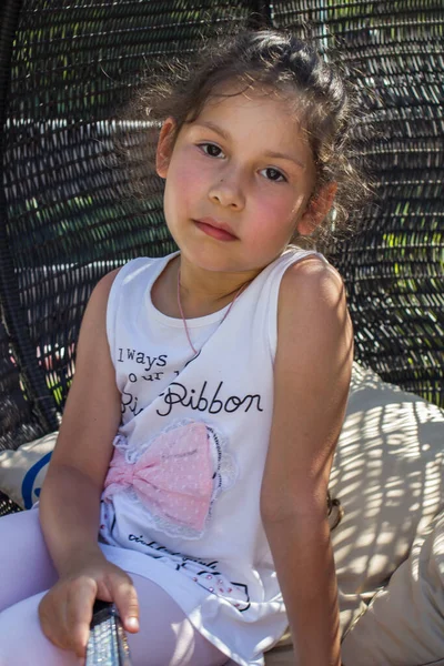 Küçük bir kız hasır bir sandalyede dinleniyor.