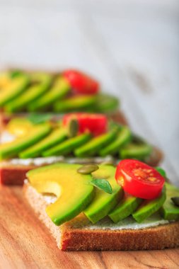 Avokado, krem peynir, tohum ve kiraz Beyaz ahşap zemin üzerine koyu siyah ekmek ekmek taze ile yapılan üzerinde avokado sandviç dilimlenmiş