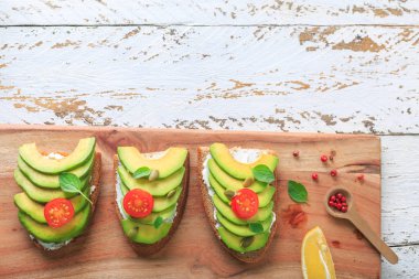 Avokado, krem peynir, tohum ve kiraz Beyaz ahşap zemin üzerine koyu siyah ekmek ekmek taze ile yapılan üzerinde avokado sandviç dilimlenmiş