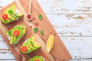 Avokado, krem peynir, tohum ve kiraz Beyaz ahşap zemin üzerine koyu siyah ekmek ekmek taze ile yapılan üzerinde avokado sandviç dilimlenmiş