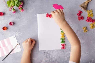 Kağıt el sanatları anneler günü, 8 Mart, Doğum günü için. Küçük çocuk bir buket çiçek renkli kağıt ve annem için renkli makarna yapıyor. Basit bir hediye fikri. kopya alanı