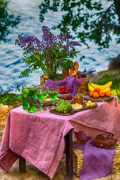 Пикник у воды за столом с цветами в лесу фрукты и овощи — стоковое фото