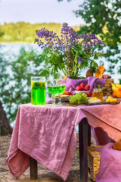 stock image picnic near water at table with flowers in forest fruits and vegetables