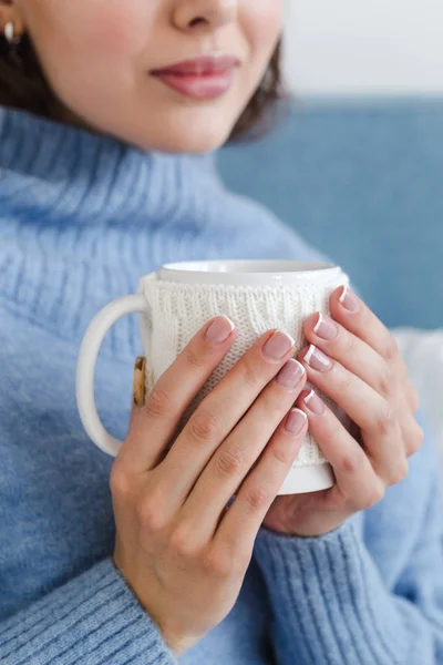 Zbliżenie dziewczyny w niebieskim swetrze z filiżanką gorącej herbaty w dłoniach — Zdjęcie stockowe