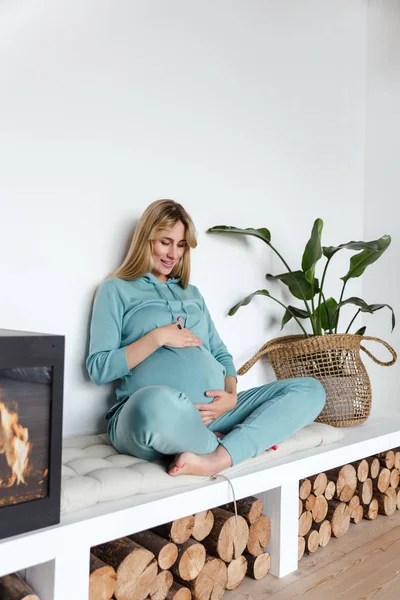 Chica embarazada en ropa deportiva verde abraza al bebé nonato y practica yoga, en un interior acogedor — Foto de Stock