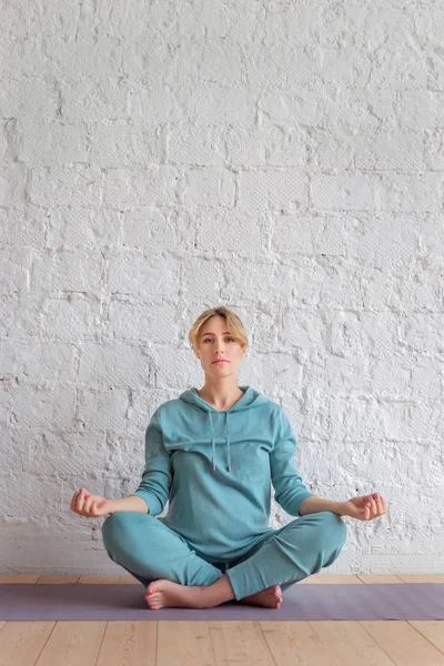 Mavi spor giyimsarışın kız lotus pozisyonda katta bir halı üzerinde oturur