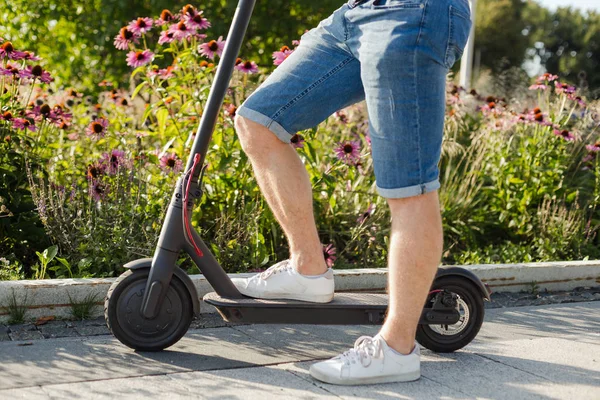 Homem montando uma scooter de pontapé elétrico eco-friendly em um parque em tempo ensolarado em calçadas — Fotografia de Stock