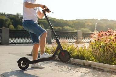 Kaldırımlarda güneşli havalarda bir parkta bir çevre dostu elektrikli kick scooter sürme Adam