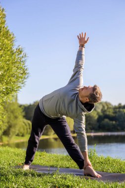 Şehir parkında yoga yapan birinden esinlendim. Spor salonu ve yaşam dengesi konsepti. Esniyorum. Üçgen Poz veya Trikonasana