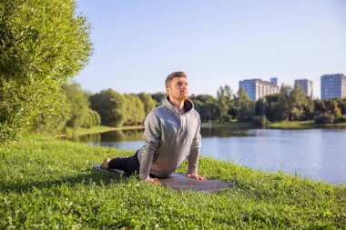 Inspired man doing yoga asanas in city park. Fitness outdoors and life balance concept.