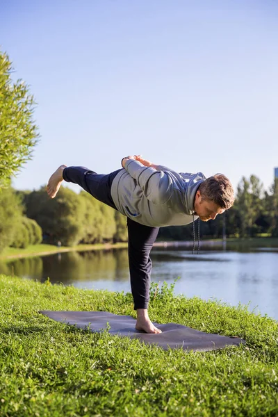 Inspired man doing yoga asanas in city park. Fitness outdoors and life balance concept.