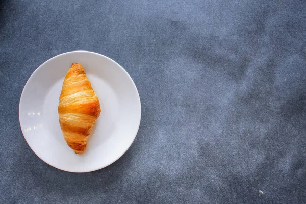 A rich variety of food photography Croissant.One delicious croissant on a dessert white plate on dark craft paper.