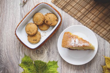 Bir fincan çay ile Erik sünger kek ve çikolata parçalı kurabiye sonbahar yaprakları çerçevede bir dilim yatak takımları bir saman üzerinde eski bir çaydanlık.
