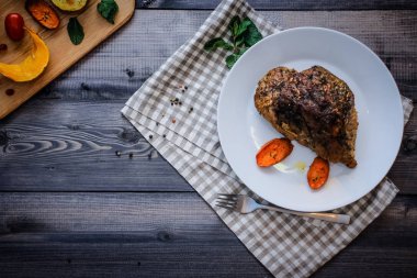 Bir beyaz tabak, çatal, kabak, patates, baharat ve kiraz domates fırında dilim yanında keten damalı peçete pişmiş havuç dilimleri ile bir parça et baharatlarla serpilir, pişmiş.