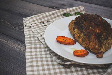 Bir parça pişmiş et ve koyu gri masa üstü bir kafeste keten peçeteye beyaz tabakta pişmiş havuç dilimleri