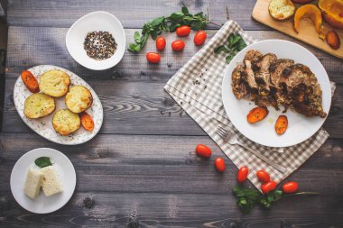 Dilimlenmiş et baharatlar, cherry domates, havuç patates yanındaki bir plaka üzerinde pişmiş tarafından çevrili bir damalı keten peçete üzerinde beyaz bir plaka üzerinde pişmiş havuç dilimleri içinde pişmiş bileşimi; Ekmek tabağı ve biber kase