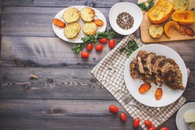 Dilimlenmiş et baharatlar, cherry domates, havuç patates yanındaki bir plaka üzerinde pişmiş tarafından çevrili bir damalı keten peçete üzerinde beyaz bir plaka üzerinde pişmiş havuç dilimleri içinde pişmiş bileşimi; Ekmek tabağı ve biber kase