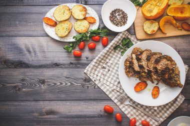 Dilimlenmiş et baharatlar, cherry domates, havuç patates yanındaki bir plaka üzerinde pişmiş tarafından çevrili bir damalı keten peçete üzerinde beyaz bir plaka üzerinde pişmiş havuç dilimleri içinde pişmiş bileşimi; Ekmek tabağı ve biber kase