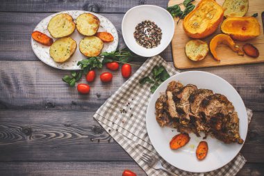 Dilimlenmiş et baharatlar, cherry domates, havuç patates yanındaki bir plaka üzerinde pişmiş tarafından çevrili bir damalı keten peçete üzerinde beyaz bir plaka üzerinde pişmiş havuç dilimleri içinde pişmiş bileşimi; Ekmek tabağı ve biber kase