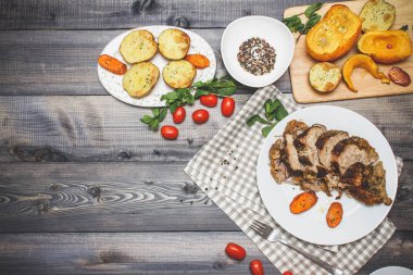 Dilimlenmiş et baharatlar, cherry domates, havuç patates yanındaki bir plaka üzerinde pişmiş tarafından çevrili bir damalı keten peçete üzerinde beyaz bir plaka üzerinde pişmiş havuç dilimleri içinde pişmiş bileşimi; Ekmek tabağı ve biber kase