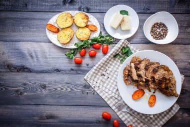 Dilimlenmiş et baharatlar, cherry domates, havuç patates yanındaki bir plaka üzerinde pişmiş tarafından çevrili bir damalı keten peçete üzerinde beyaz bir plaka üzerinde pişmiş havuç dilimleri içinde pişmiş bileşimi; Ekmek tabağı ve biber kase