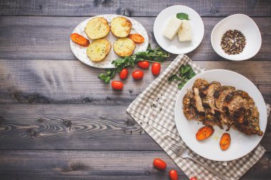 Dilimlenmiş et baharatlar, cherry domates, havuç patates yanındaki bir plaka üzerinde pişmiş tarafından çevrili bir damalı keten peçete üzerinde beyaz bir plaka üzerinde pişmiş havuç dilimleri içinde pişmiş bileşimi; Ekmek tabağı ve biber kase