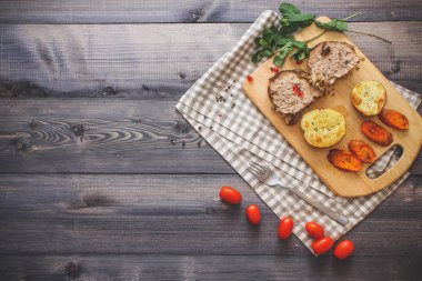 Kesme tahtası üzerinde pişmiş et iki dilim, iki dilim patates ve havuç dilimleri, keten, kareli bir peçete pişmiş bir kapta çok renkli bezelye biber ve grafit tezgahı çerçevede bir tabakta kesilmiş bir nar vardır