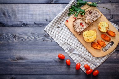 Kesme tahtası üzerinde pişmiş et iki dilim, iki dilim patates ve havuç dilimleri, keten, kareli bir peçete pişmiş bir kapta çok renkli bezelye biber ve grafit tezgahı çerçevede bir tabakta kesilmiş bir nar vardır