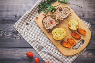 Kesme tahtası üzerinde pişmiş et iki dilim, iki dilim patates ve havuç dilimleri, keten, kareli bir peçete pişmiş bir kapta çok renkli bezelye biber ve grafit tezgahı çerçevede bir tabakta kesilmiş bir nar vardır