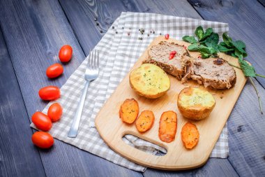 Kesme tahtası üzerinde pişmiş et iki dilim, iki dilim patates ve havuç dilimleri, keten, kareli bir peçete pişmiş bir kapta çok renkli bezelye biber ve grafit tezgahı çerçevede bir tabakta kesilmiş bir nar vardır