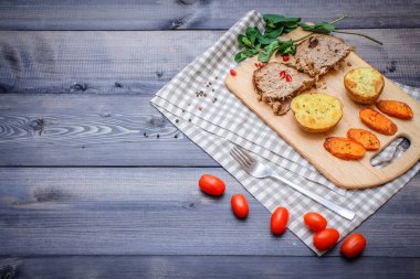 Kesme tahtası üzerinde pişmiş et iki dilim, iki dilim patates ve havuç dilimleri, keten, kareli bir peçete pişmiş bir kapta çok renkli bezelye biber ve grafit tezgahı çerçevede bir tabakta kesilmiş bir nar vardır