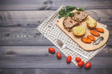 Kesme tahtası üzerinde pişmiş et iki dilim, iki dilim patates ve havuç dilimleri, keten, kareli bir peçete pişmiş bir kapta çok renkli bezelye biber ve grafit tezgahı çerçevede bir tabakta kesilmiş bir nar vardır