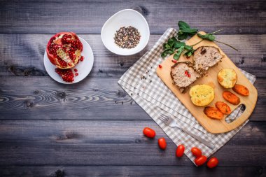 Kesme tahtası üzerinde pişmiş et iki dilim, iki dilim patates ve havuç dilimleri, keten, kareli bir peçete pişmiş bir kapta çok renkli bezelye biber ve grafit tezgahı çerçevede bir tabakta kesilmiş bir nar vardır