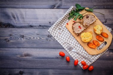 Kesme tahtası üzerinde pişmiş et iki dilim, iki dilim patates ve havuç dilimleri, keten, kareli bir peçete pişmiş bir kapta çok renkli bezelye biber ve grafit tezgahı çerçevede bir tabakta kesilmiş bir nar vardır