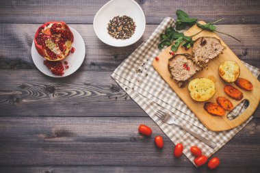 Kesme tahtası üzerinde pişmiş et iki dilim, iki dilim patates ve havuç dilimleri, keten, kareli bir peçete pişmiş bir kapta çok renkli bezelye biber ve grafit tezgahı çerçevede bir tabakta kesilmiş bir nar vardır