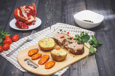 Kesme tahtası üzerinde pişmiş et iki dilim, iki dilim patates ve havuç dilimleri, keten, kareli bir peçete pişmiş bir kapta çok renkli bezelye biber ve grafit masa üstü karşı bir tabakta kesilmiş bir nar vardır