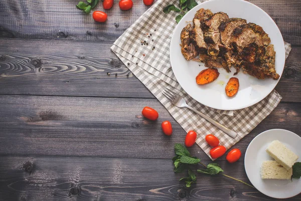 Dilimlenmiş et baharatlar, cherry domates, havuç patates yanındaki bir plaka üzerinde pişmiş tarafından çevrili bir damalı keten peçete üzerinde beyaz bir plaka üzerinde pişmiş havuç dilimleri içinde pişmiş bileşimi; Ekmek tabağı ve biber kase