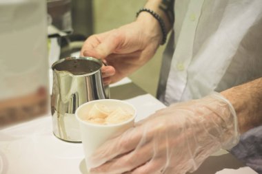 Bir adam beyaz marshmallow ile hava su bardağı kakao dökülüp sıcak içki hazırlar.