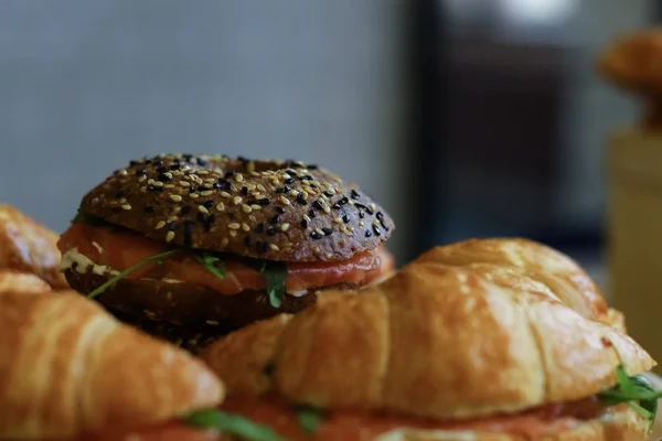 サーモンとレタスの充填を見ることができる暗いハンバーガー サンドイッチ広がって周り葉します — ストック写真