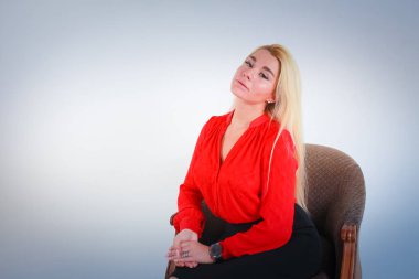 Beyaz ışık Mavi degrade arka plan için. Bir kız geri atılmış bir kırmızı bluz kafasında bir sandalye derslerde bileğini sert oturur.