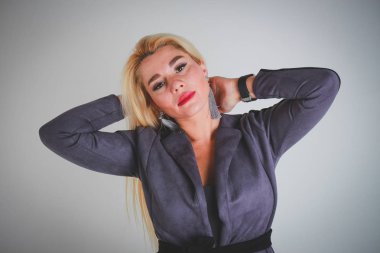 Beyaz ışık gri degrade arka plan. Gri ceket office tarzında kız kamera Eller başının arkasına bakıyor.