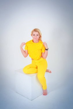 Beyaz ışık Mavi degrade arka plan için. Beyaz bir küp oturur sarı pantolon ile sarı bir gömlek bir kız onun tişörtünü düzeltiyor.